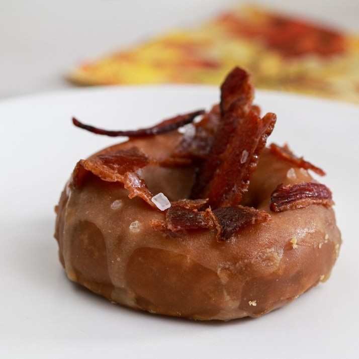 gluten-free maple glazed donut on white plate topped with bacon maple syrup & salt
