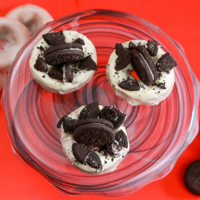 Vanilla gluten-free donut topped with crushed KinniTOOS chocolate cookies on red background