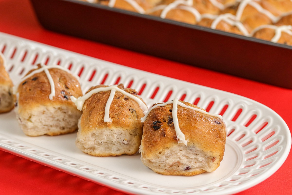 Gluten-free Hot Cross Buns on white latticed dish red table, pan in background