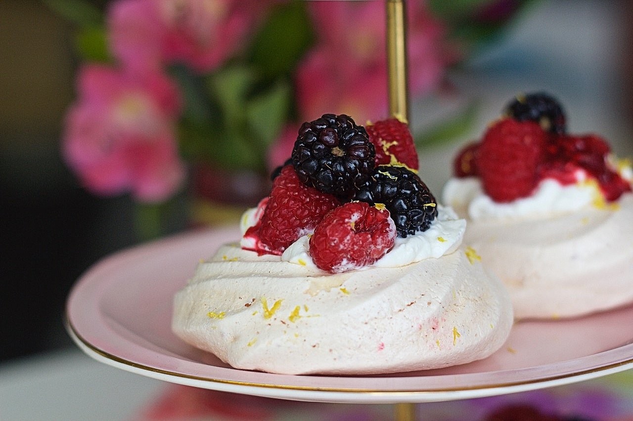 Gluten-free meringue cloud with berries on top on white plate, out of focus flowers in background