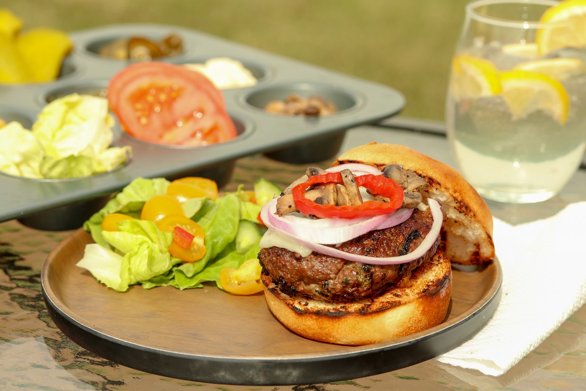 Gluten-free hamburger bun filled with beef patty bocconcini on wooden table with summer drink