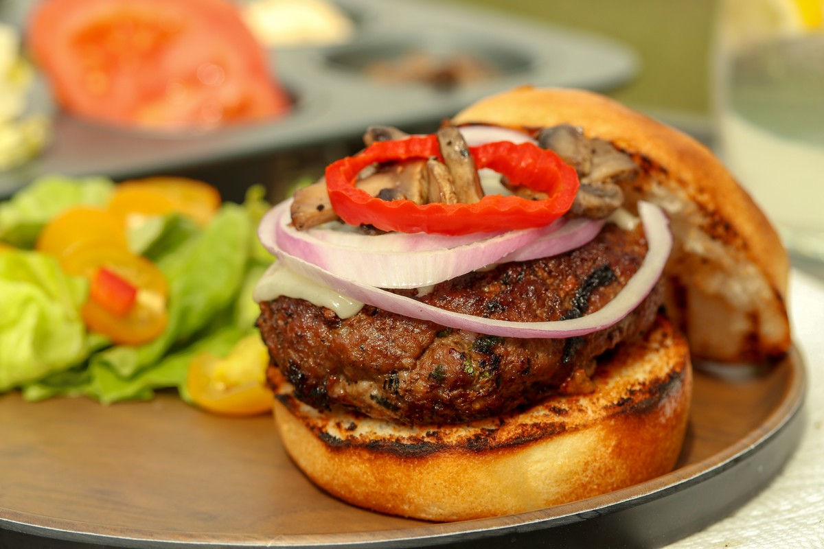 Gluten-free hamburger bun filled with beef patty bocconcini on wooden table with summer drink