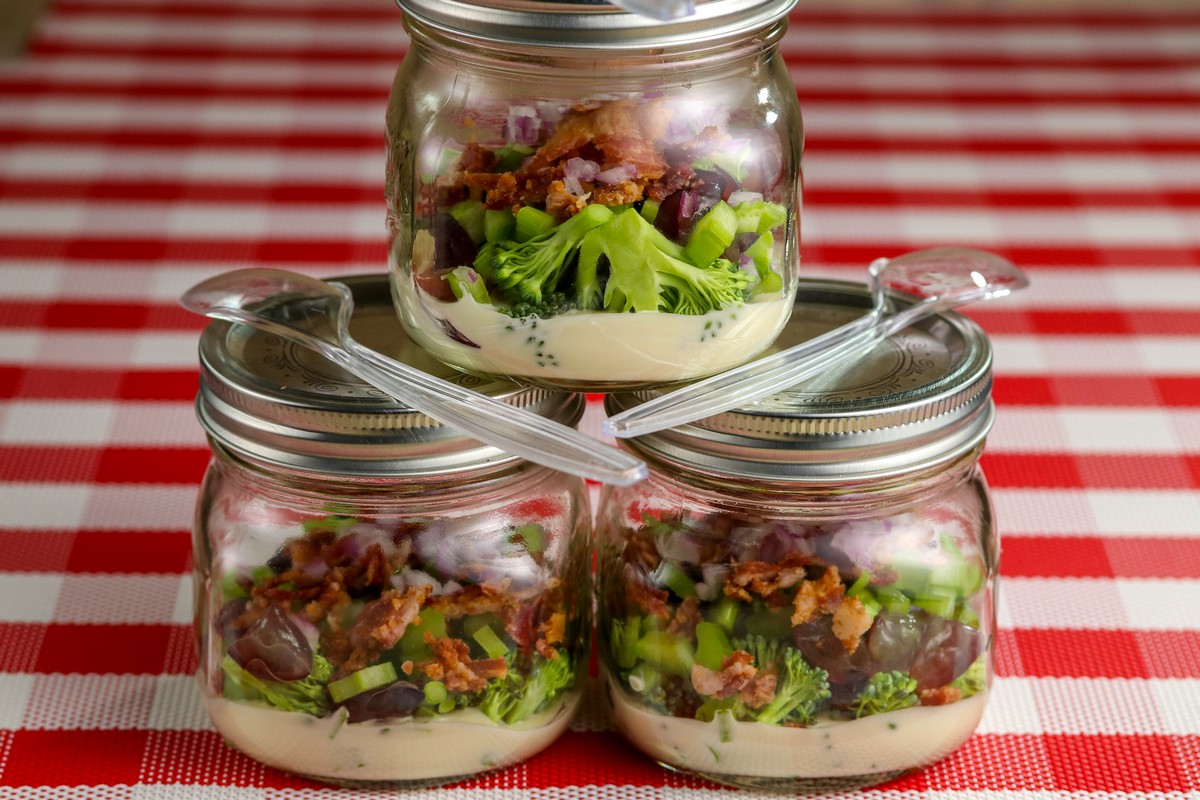 Broccoli Bacon Salad in three glass mason jars with lids on red & white chequered table cloth