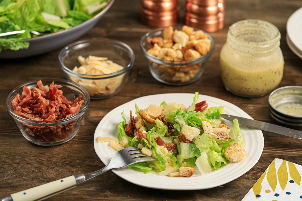 Gluten-free croutons on top of Caesar Salad on white plate on wooden table with cutlery 