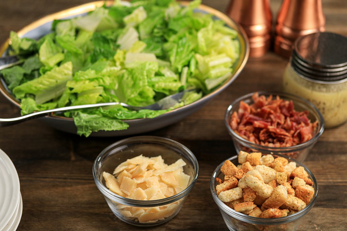 Ingredients for gluten-free Caesar Salad on wooden board in glass bowls, lettuce, parmesan, bacon bits, dressing