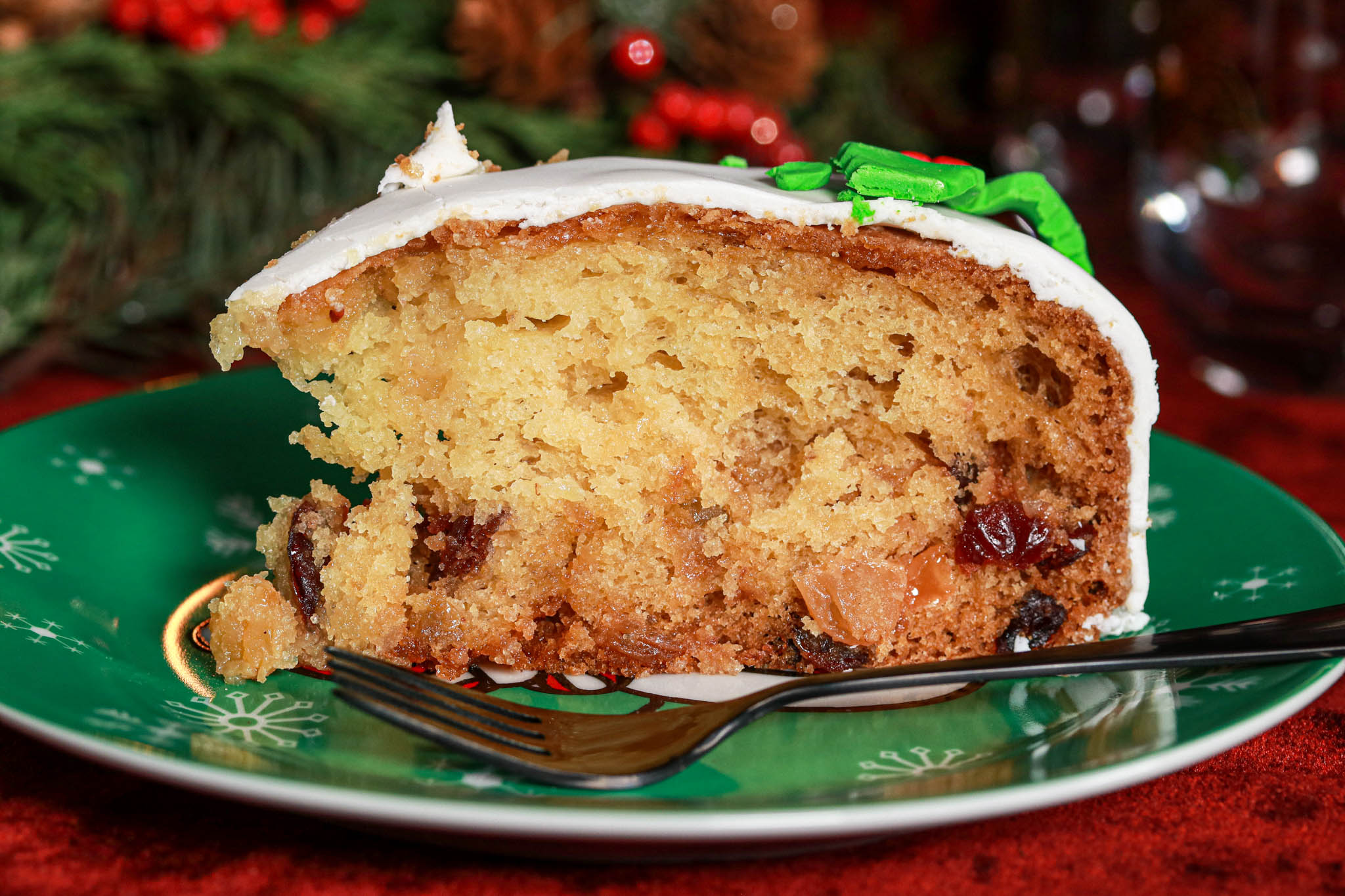 Festive Christmas gluten free slice of cake on green plate, red velvet tablecloth, baubles decorating 