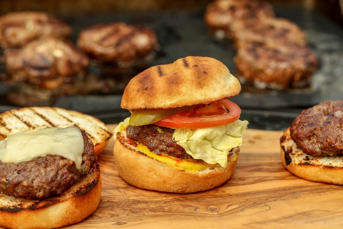 Gluten-free hamburger bun filled with beef patty, on wooden table BBQ in background