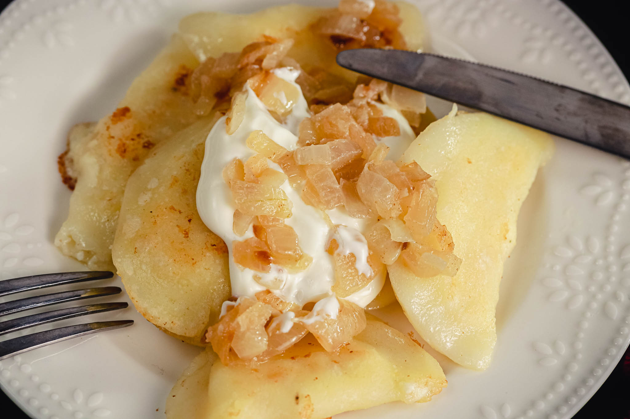 Gluten-free cottage cheese potato onion pierogi on traditional Ukrainian serving dish surrounded by others on board. 