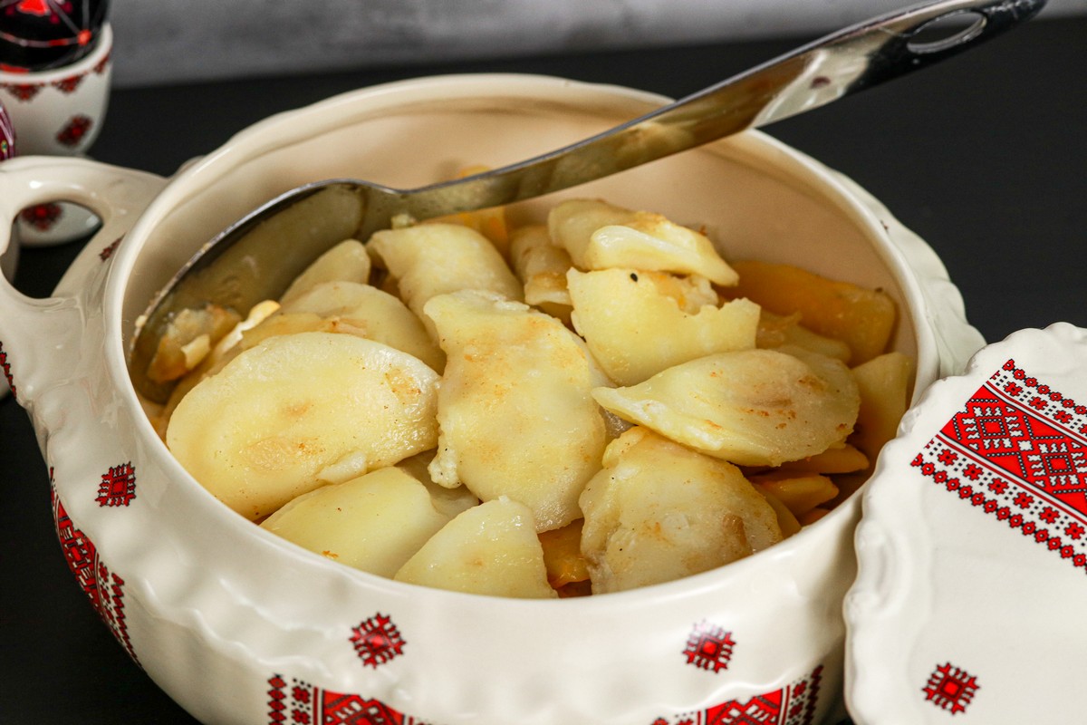 Gluten-free cottage cheese potato onion pierogi on traditional Ukrainian serving dish surrounded by others on board. 