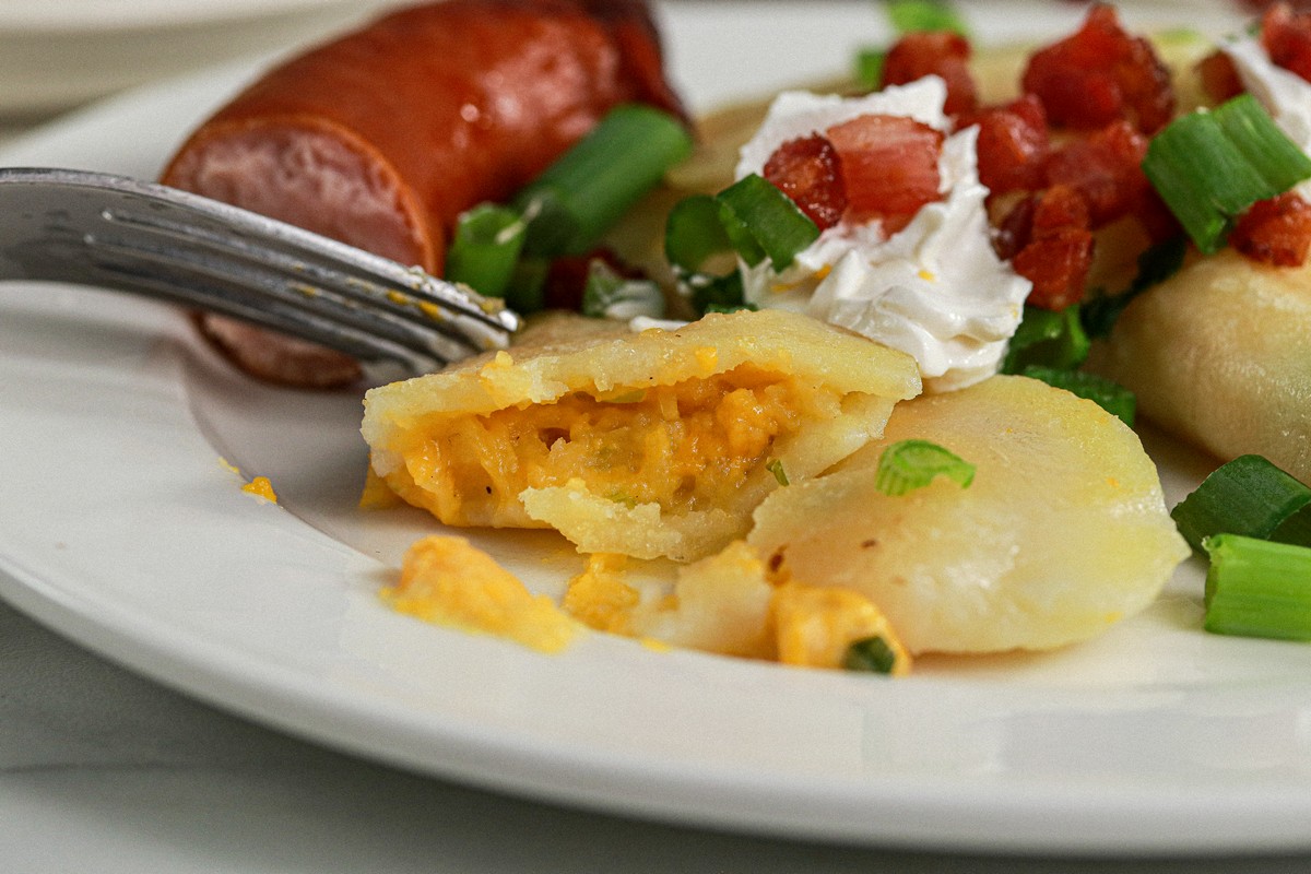 Close up Gluten & Dairy Free Pierogi cut open on Ukrainian serving dish surrounded by Ukrainian dishes