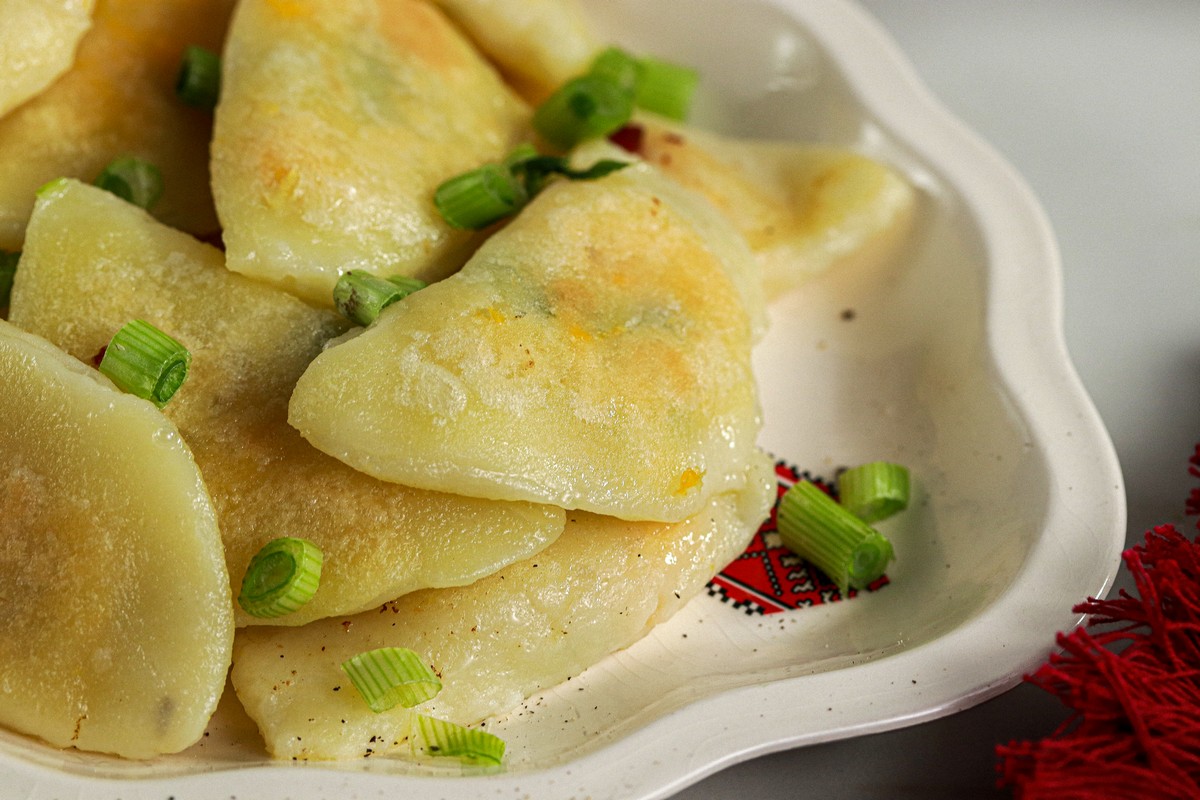 Close up dough Gluten & Dairy Free Pierogi on Ukrainian serving dish surrounded by Ukrainian dishes