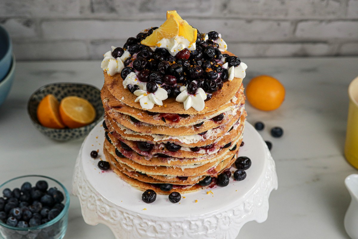 Gluten-free Lemon Blueberry Torte on white stand, white brick background