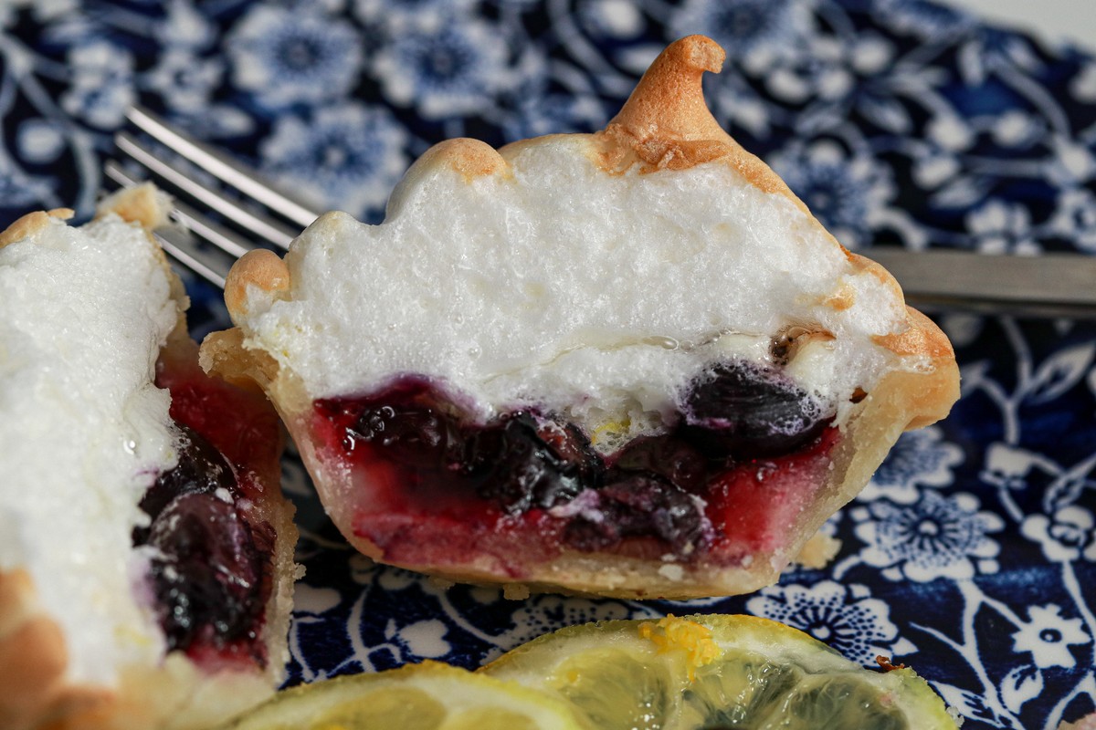Gluten-free meringue blueberry tarts cut in half on a blue white plate