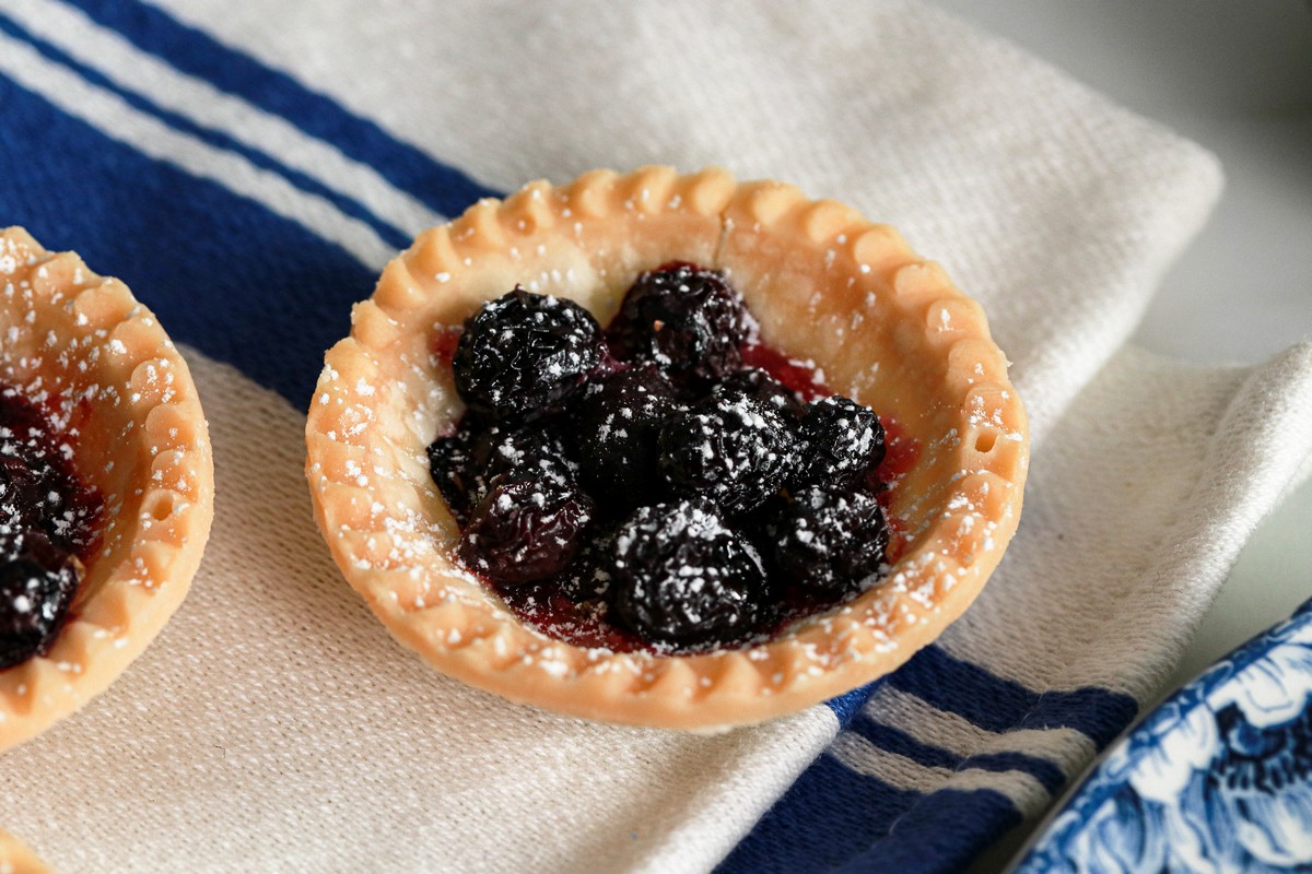 Gluten-free tart shell filled with blueberries on a blue and white kitchen towel