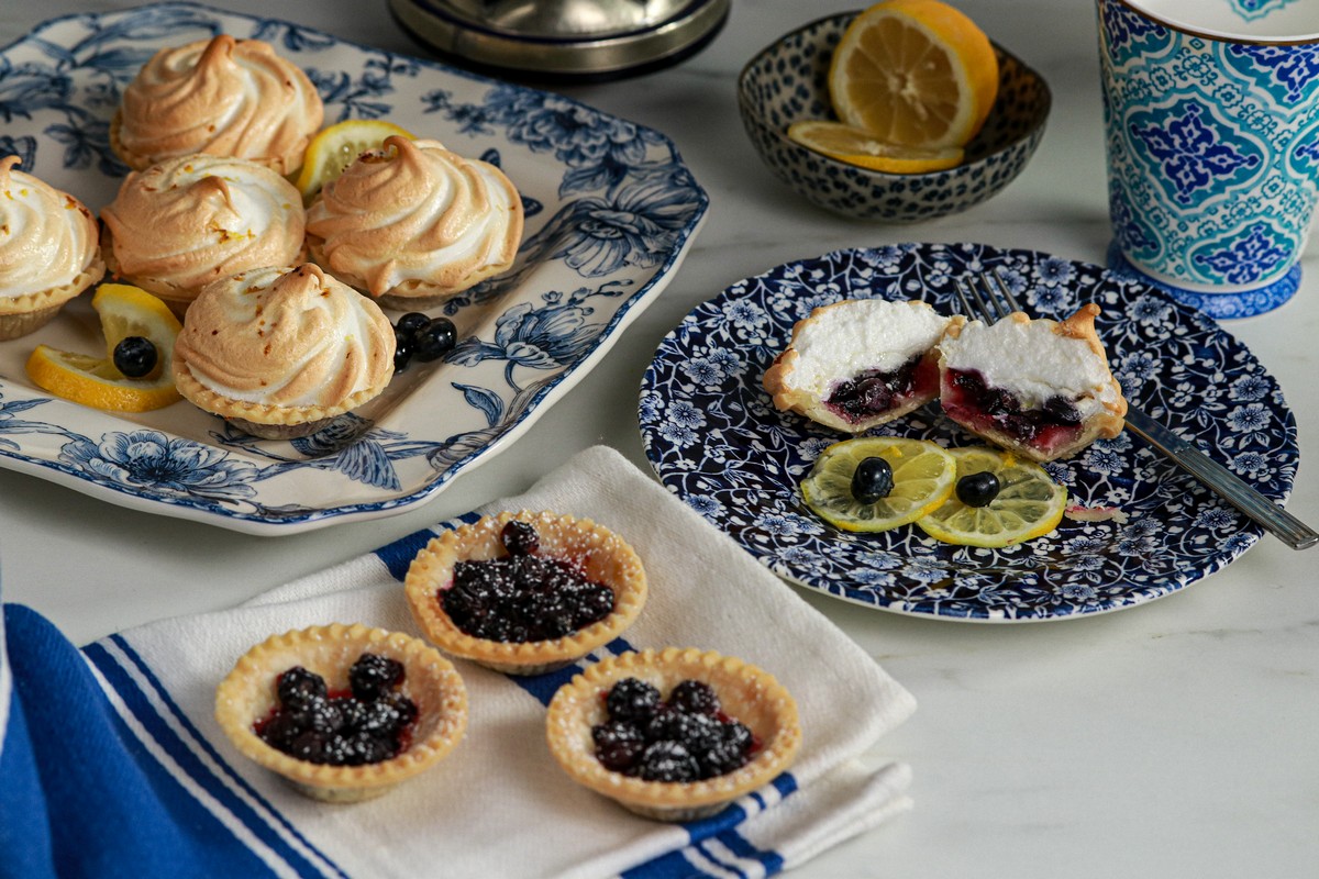 Gluten-free meringue tarts in various stages of assembly on blue/white plates, with a towel, one half cut