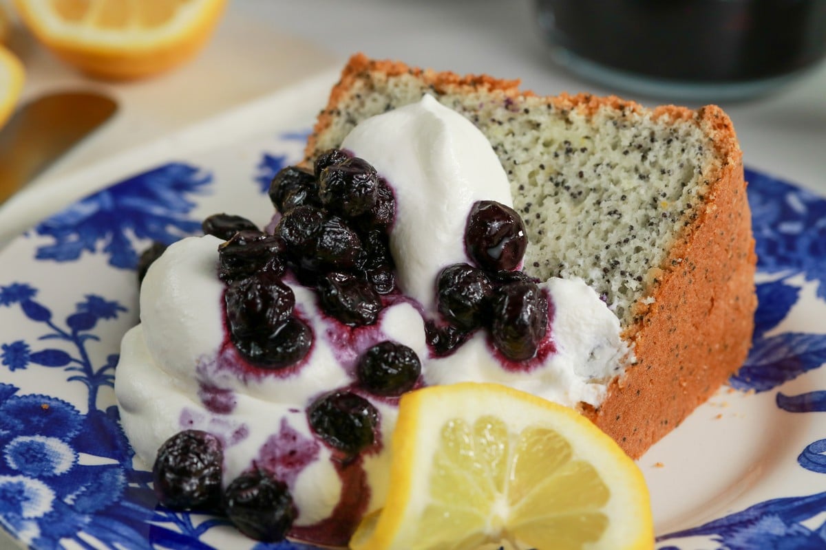 Gluten-free Lemon Poppy Seed Cake covered in cream & blueberries on a blue & white plate