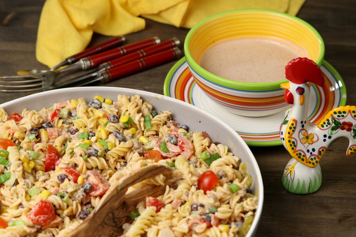 Mexican Pasta Salad in brighly coloured bowl on wooden board surrounded by bright ceramic pottery