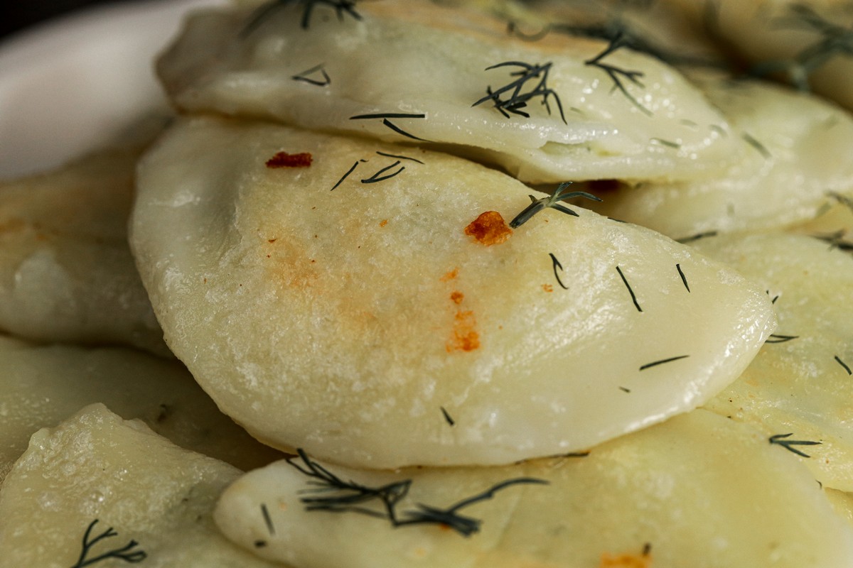 Gluten-free Pierogies made with cheese dill & potato on Ukrainian serving dish close up. 