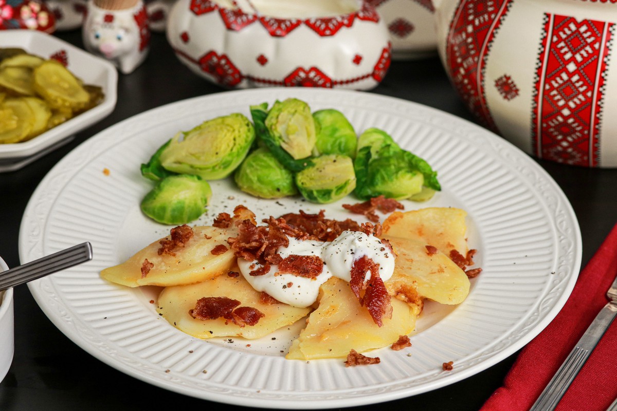 Gluten-free cheddar bacon pierogies on plate surrounded byUkrainian dishes