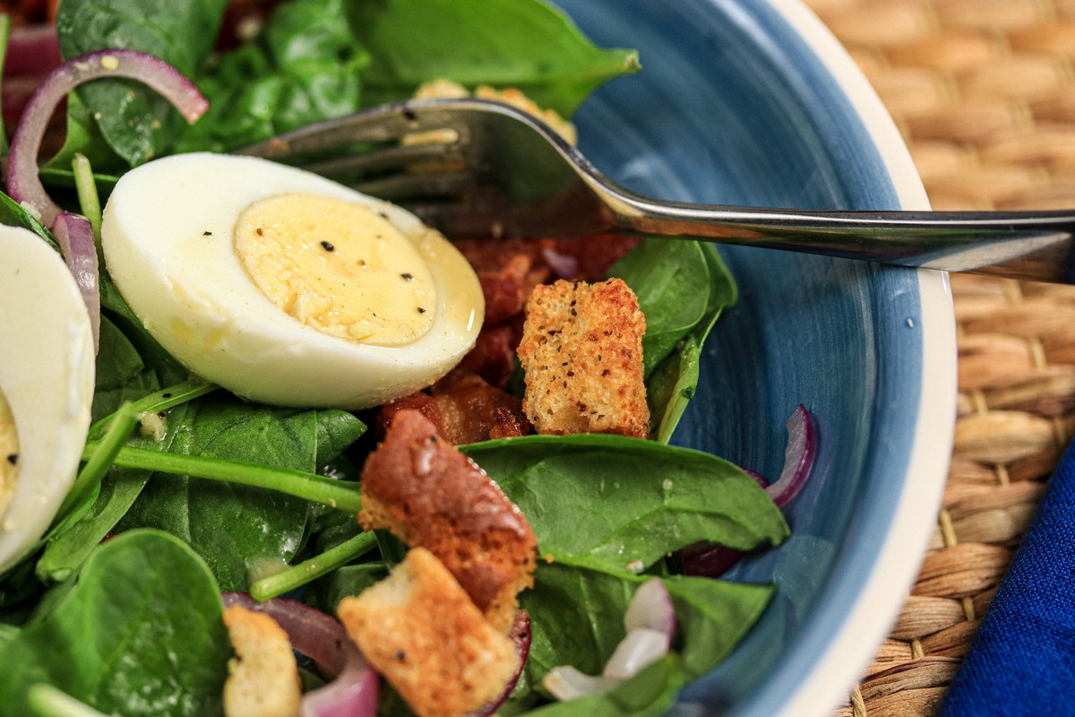 gluten-free croutons on egg bacon spinach salad in blue plate on straw mat