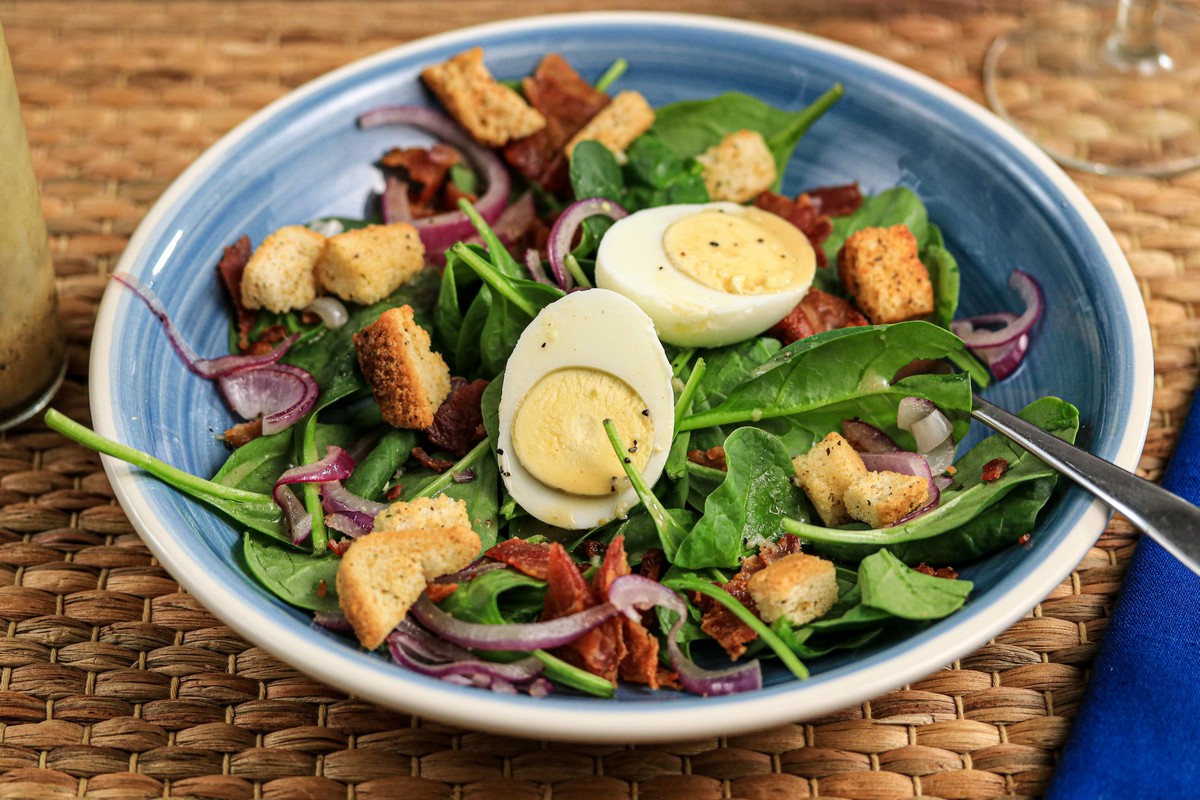 Gluten-free croutons on egg spinach salad in blue bowl on straw mat