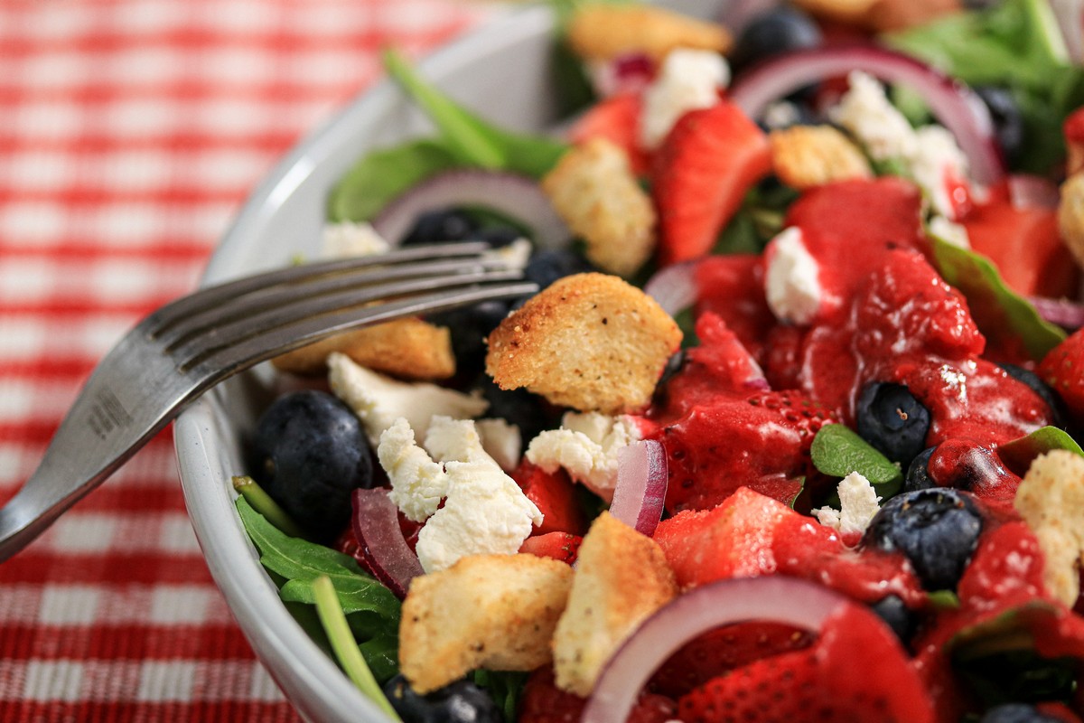 Gluten-free Arugula Berry Salad in bowl on red & white chequered table cloth