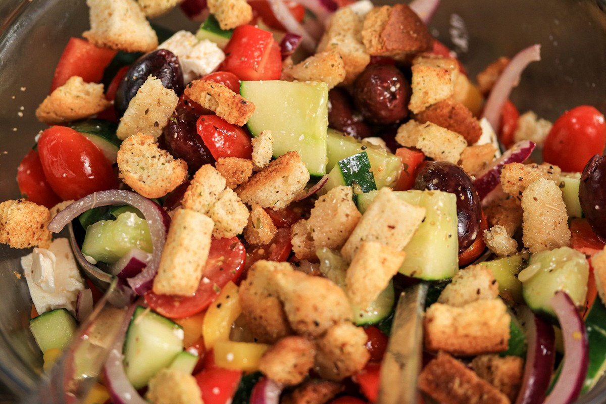 Gluten-free croutons in Greek Salad in a glass bowl on a wooden kitchen top