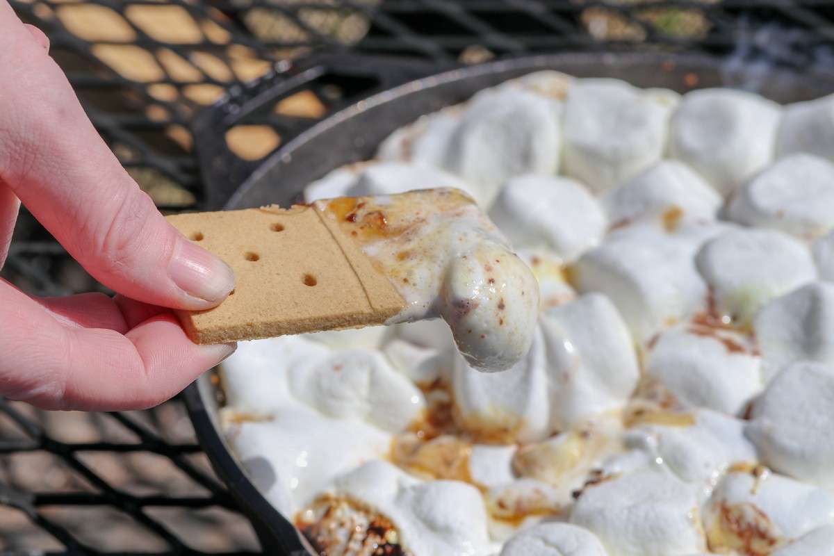 Dipping smoreables into skillet of melted marshallows on firepit